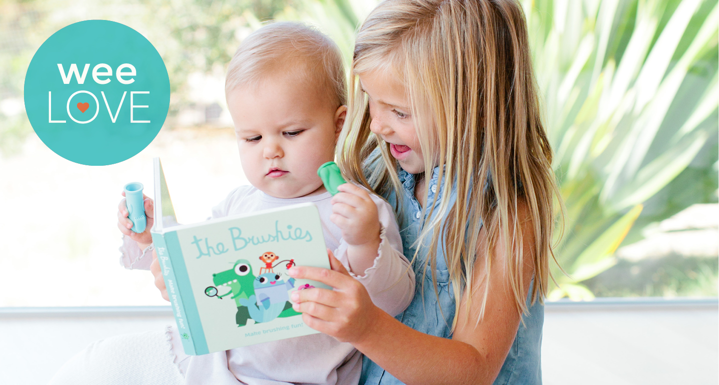 Girl reads Brushies book to baby while baby holds toothbrush.